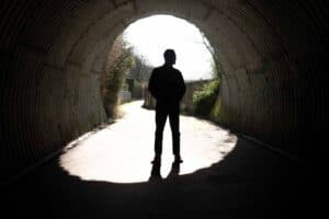Silhouette of a person standing in the middle of a tunnel, facing the bright daylight outside. The light creates a contrast between the dark interior and the illuminated exterior, highlighting the person's outline—a moment captured perfectly in Manchester's vibrant music and comedy scene.