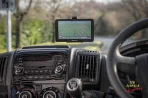 The image, captured by an Oldham photographer, shows the interior of a vehicle with a GPS navigation system mounted on the dashboard. The GPS screen displays a map and directions. The steering wheel and parts of the dashboard, including air vents and control knobs, are visible.