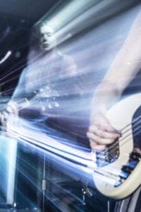 An Oldham photographer captures a dynamic image of two musicians performing, with one playing a guitar and the other a bass. The scene features motion blur and streaks of light, creating a sense of energy and movement. The dark background enhances the visual effect of the lights.