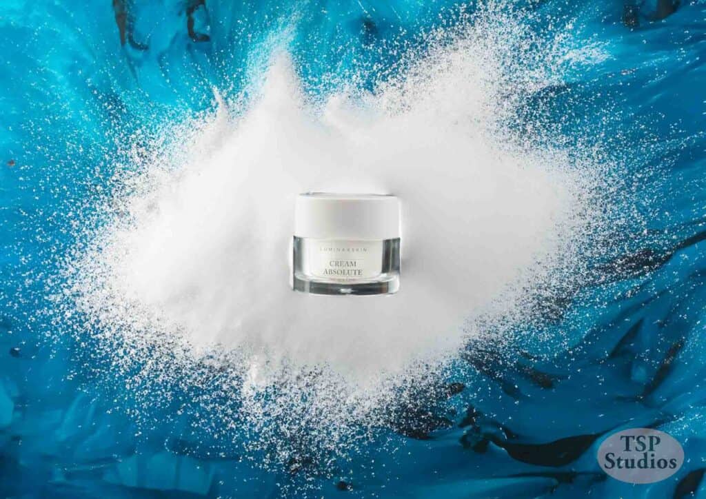 A jar of cream is placed at the center of a splatter of white powder on a vibrant blue marbled background. The jar's label reads "Cream Absolute." The bottom right corner features the text "TSP Studios" in a translucent oval shape.