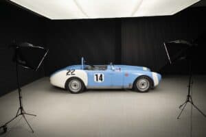 A vintage blue and white race car with the number 14 on its side sits under studio lighting, with two light stands positioned on each side against a dark background.