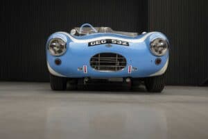 A vintage blue race car with the license plate "GEG 532" is parked in front of a black corrugated wall. The car features a central grille and prominent headlights.