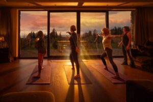 Four people practice yoga indoors on mats in front of large windows, with warm sunlight streaming in at sunset, illuminating the room and casting long shadows on the floor.