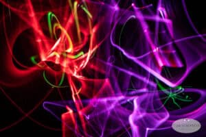 Colorful abstract light trails in swirling patterns of red, pink, purple, and green on a black background, creating a vibrant and energetic visual effect.