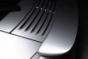 Close-up of the rear section of a silver sports car, showing the engine cover with multiple air vents and part of the rear spoiler in soft lighting.