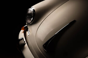 Close-up of the front left side of a classic porsche 356 cream-colored car, showing the headlight, indicator, and curved chrome details against a dark background. shot using the FDL technique