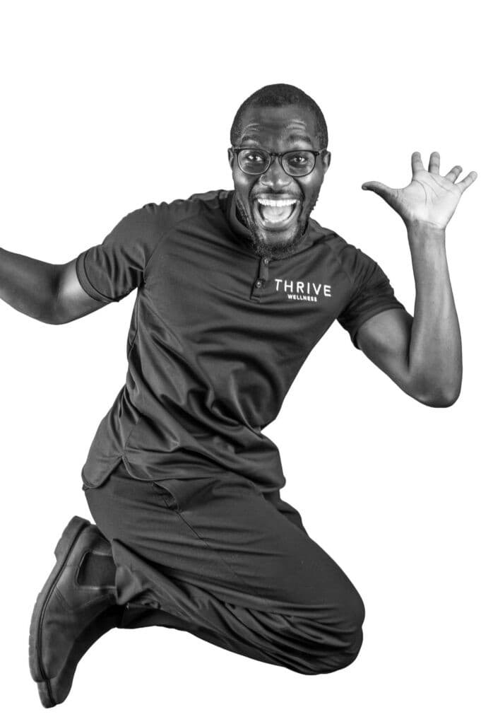A man wearing glasses and a "Thrive" shirt jumps in the air excitedly, smiling widely with hands raised, against a white background.