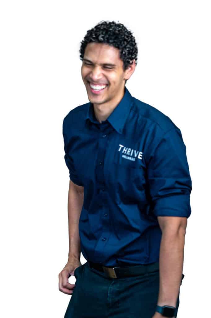 A man wearing a navy blue "THRIVE" button-up shirt is smiling and laughing, standing against a plain white background.