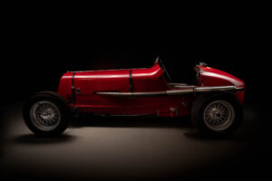 A classic vintage red ERA racing car with exposed wheels and a single seat, shown in profile view against a dark background.