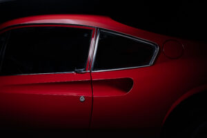 Close-up of the side of a red ferrari dino sports car, showing the door, window, and part of the rear with sleek curves and shiny chrome trim, set against a dark background photographed using the fdl technique